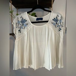 White blouse with blue floral detail on the shoulder